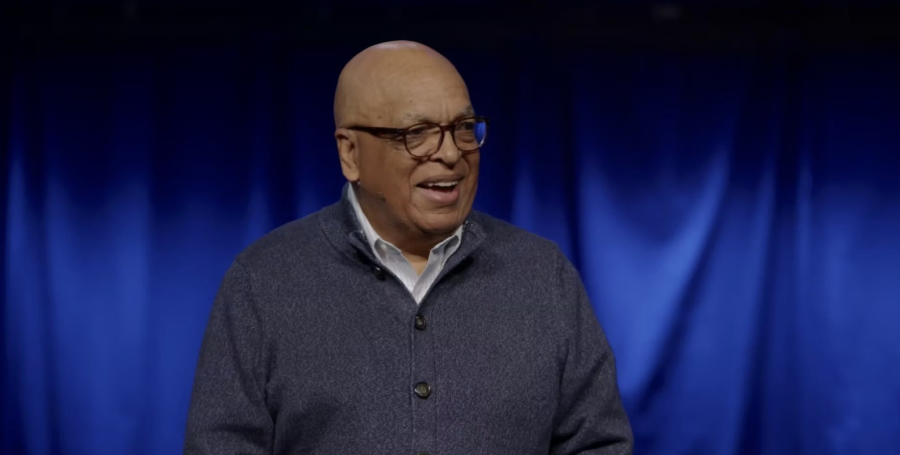 African American gentleman preaching in front of a blue background