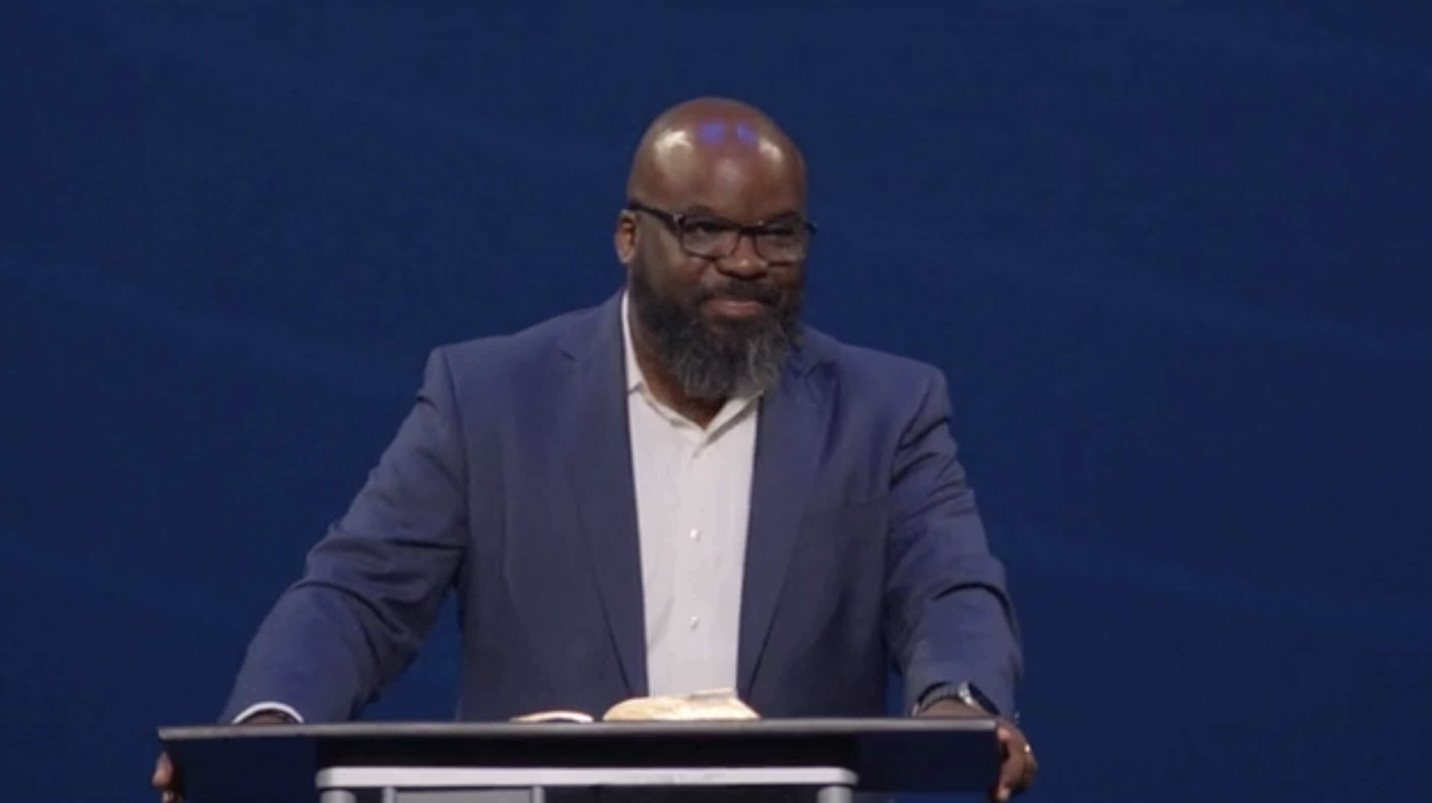 Bald African-American gentleman with beard standing in front of a pulpit with the Bible open