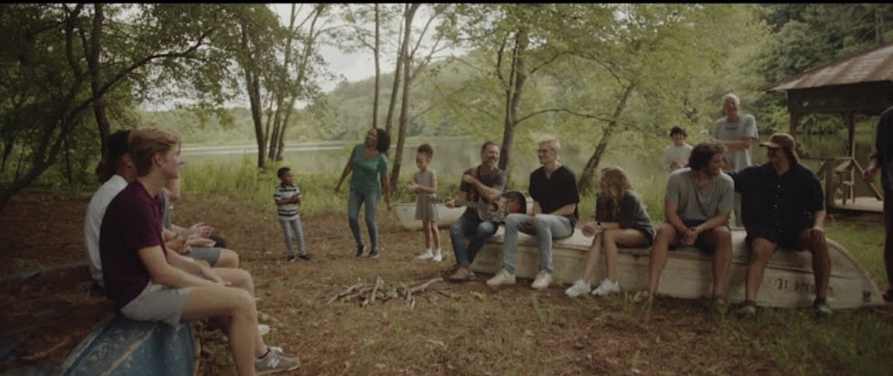 young adults sitting on benches outside by a river under trees