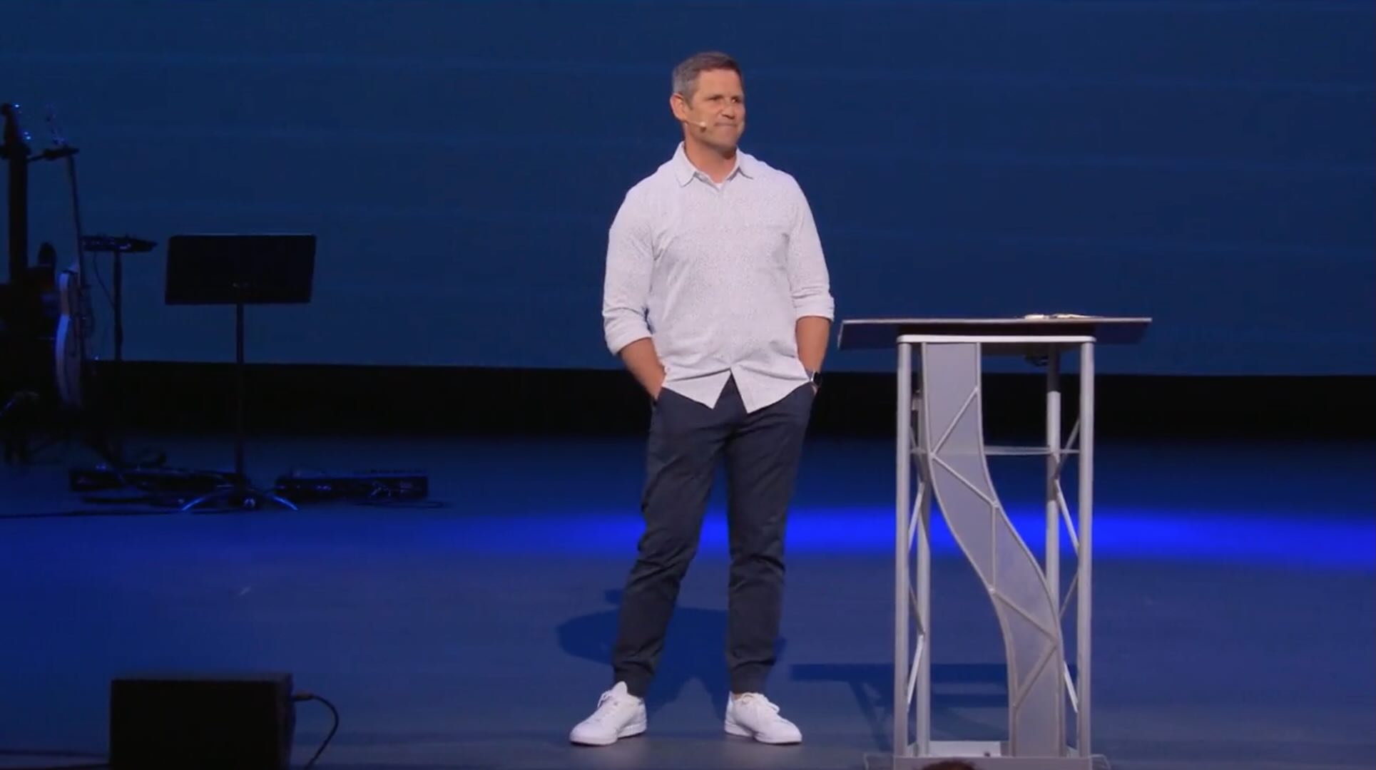 man in white shirt and white shoes standing next to a pulpit