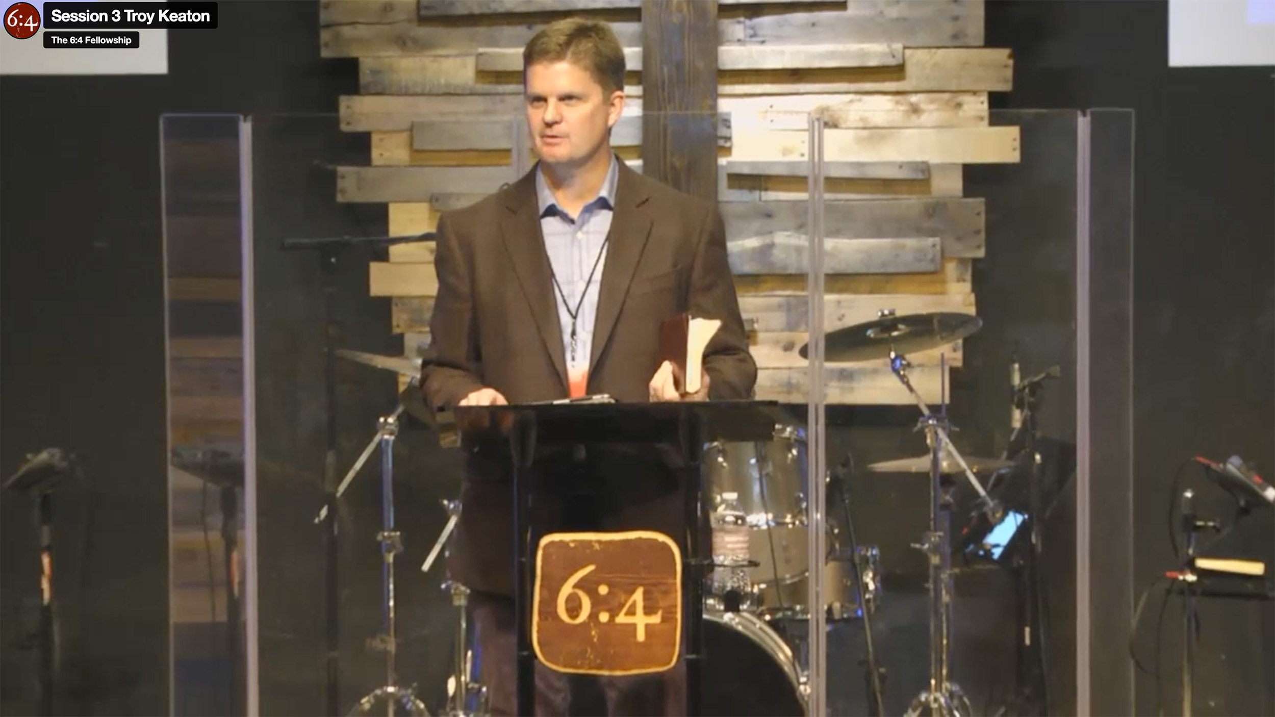 Man speaking at a podium with drums behind.