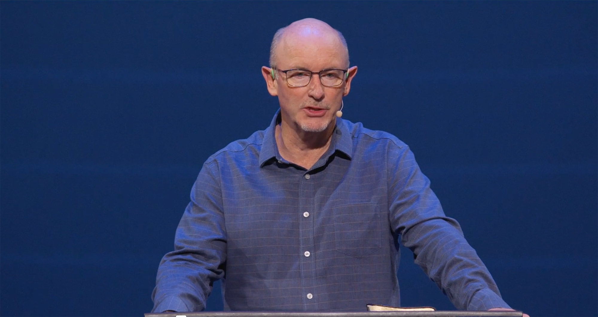 Man speaks on stage with blue background.