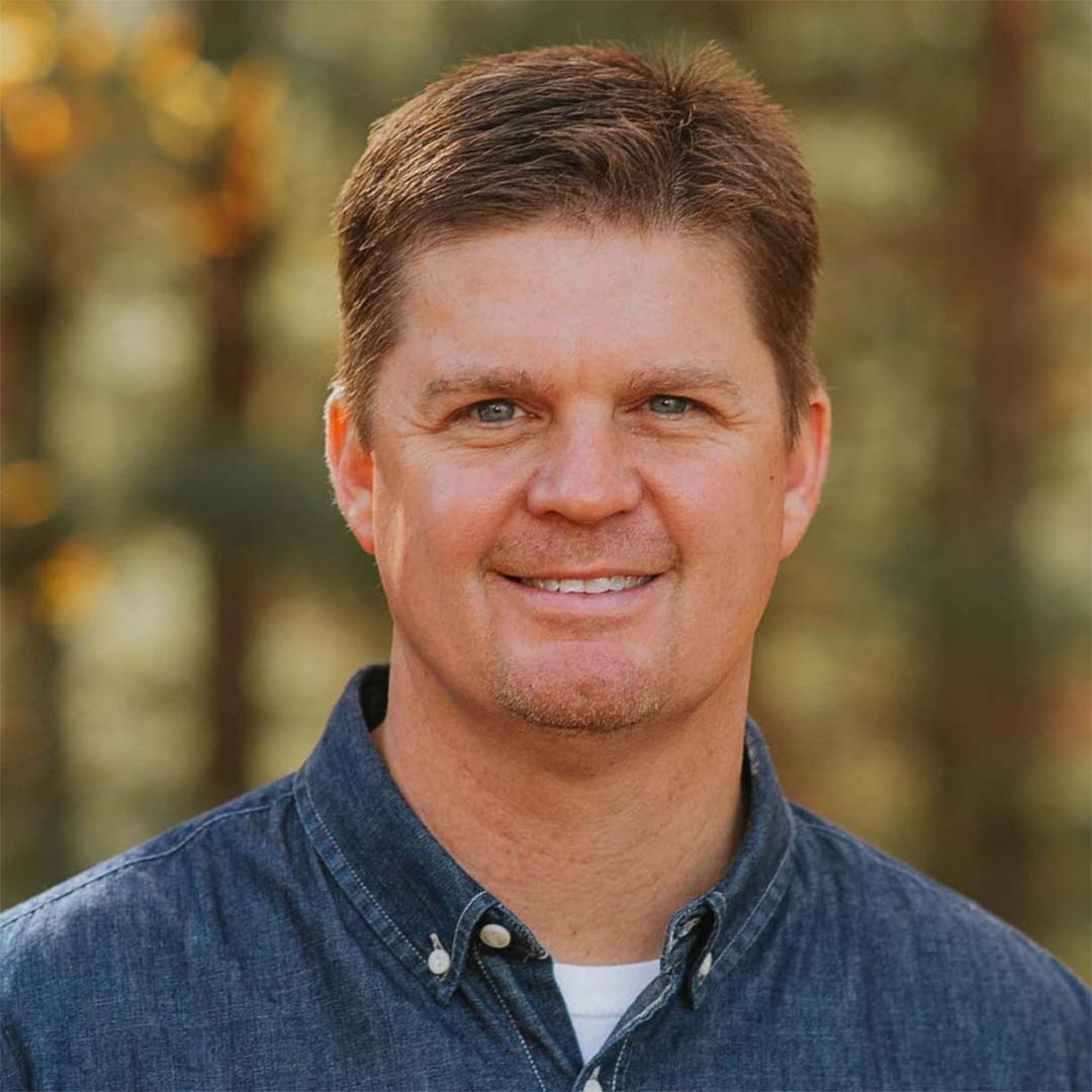 Troy Keaton smiling in denim shirt outdoors