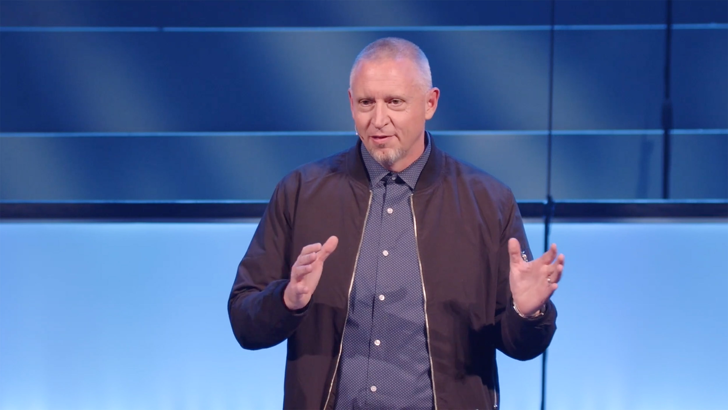 Speaker presenting on stage with blue background.